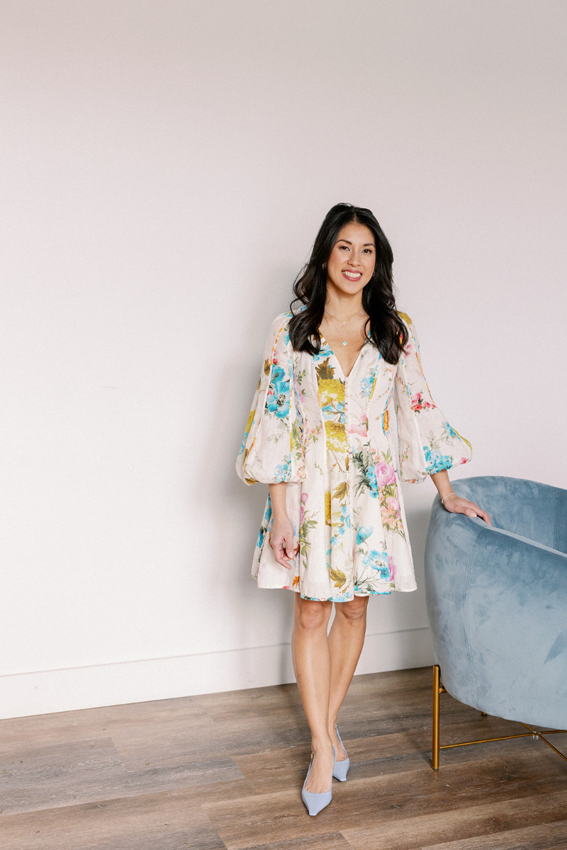 Desirée Adams stands against white wall with velvet baby blue chair next to her as she explains how attracting clients for full-service weddings isn't about readiness but about systems and confidence.