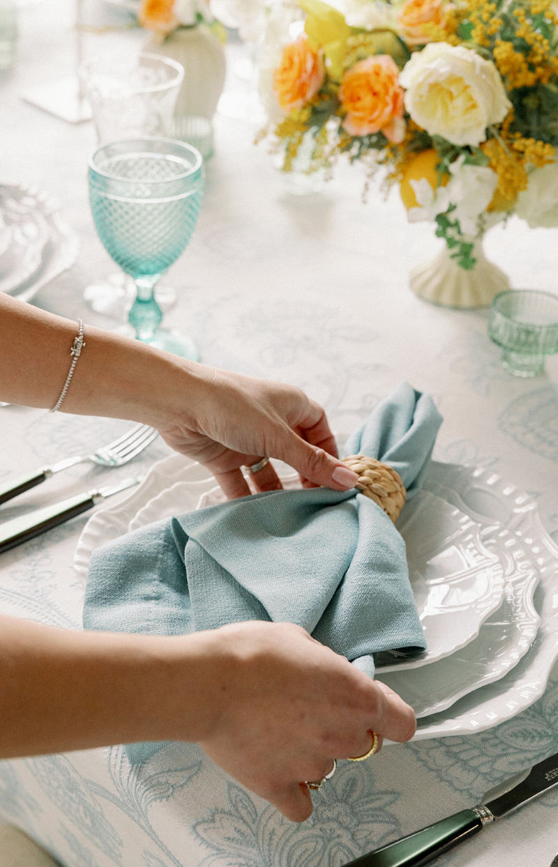 Desirée Adams places folded napkin with rattan ring on white china for wedding table setting as she talks about post-engagement season marketing.