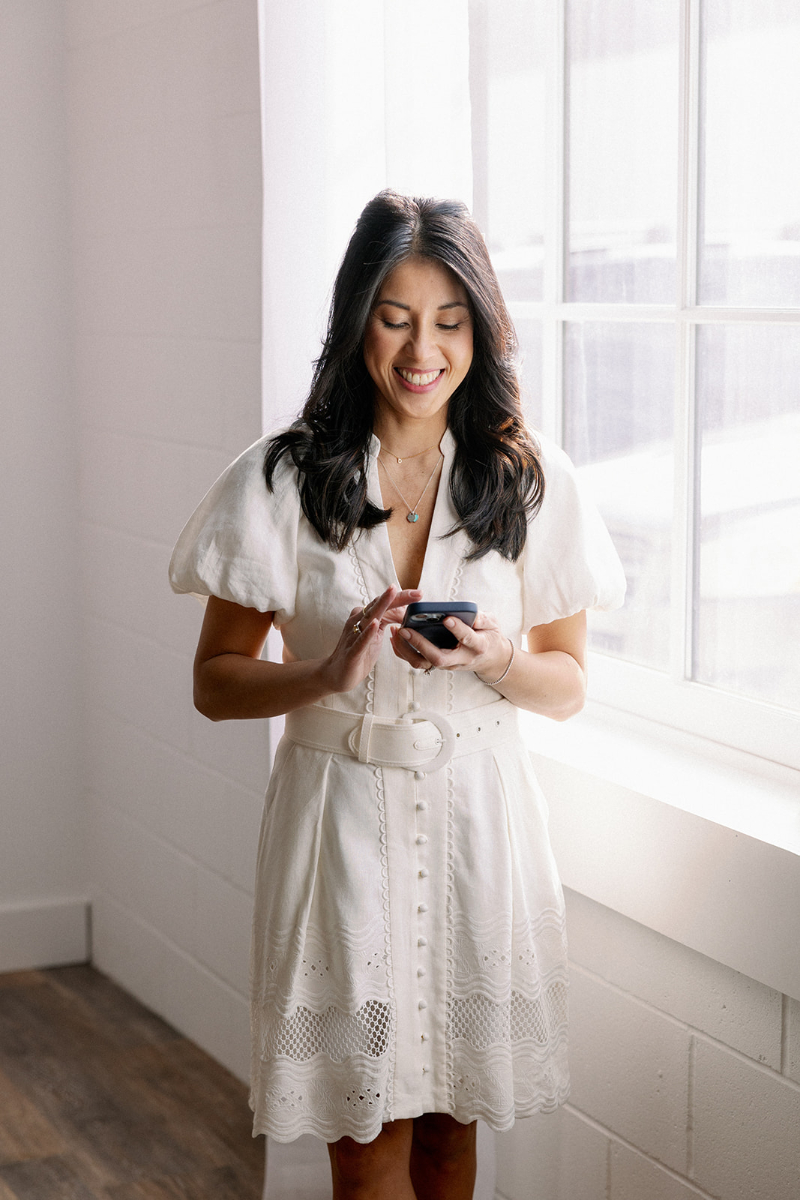 Desirée Adams stands next to bright window as she texts a fellow planner about the subtle marketing signals that attract the right clients.
