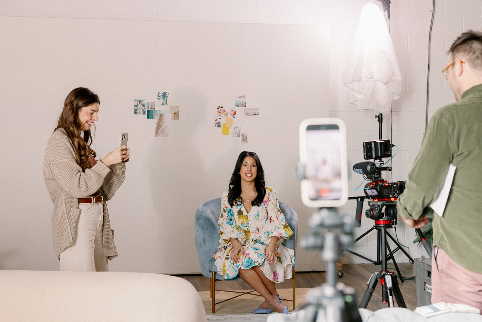 Desirée Adams sits in blue chair as woman stands recording her with an iphone, another phone recording her in the distance as she records an episode about the social media trends wedding planners should pay attention to in 2026.