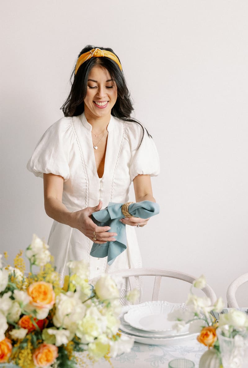 Desirée Adams poses during styled shoots for Verve Event Co. as she holds a folded napkin and places it on the decorated tablescape.